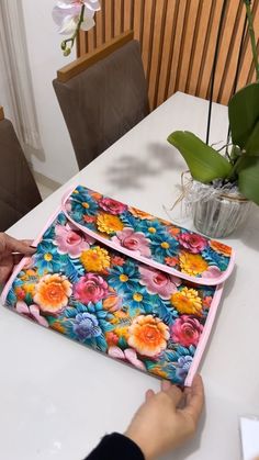 a person is working on a colorful flowered bag at a table with flowers in the background