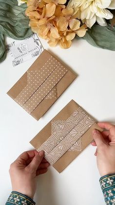 someone cutting out some brown paper on top of a white table with flowers in the background