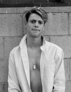 black and white photograph of a shirtless man leaning against a brick wall with his hands in his pockets