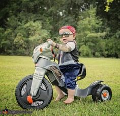 a toddler riding on the back of a motorcycle with an adult pointing at it