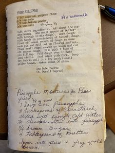 an old book with writing on it sitting on top of a wooden table next to a pen