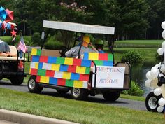 two people riding in a colorful cart with balloons and streamers on the side walk