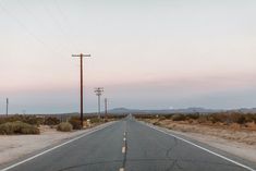 an empty road in the middle of nowhere with telephone poles and power lines on either side