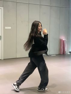 a woman in black shirt and grey pants dancing with her hands up to the side