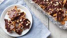 chocolate and almond brittles on a white plate next to a blue napkin with a piece of tin foil