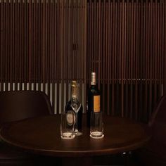 two bottles of wine sitting on top of a wooden table next to brown leather chairs