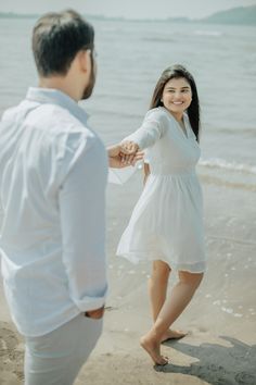 a man and woman holding hands on the beach