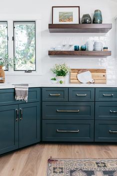 a kitchen with blue cabinets and wooden shelves on the wall, along with an area rug