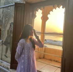 a woman standing in front of a window looking out at the ocean