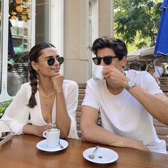 a man and woman sitting at a wooden table with cups of coffee in front of them