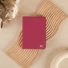 a pink book sitting on top of a wooden plate next to flowers and a vase