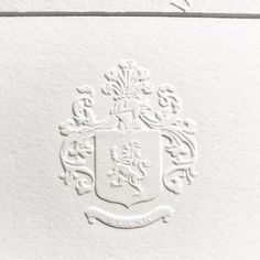 an ornate crest on the back of a letterpressed wedding card, printed in white paper