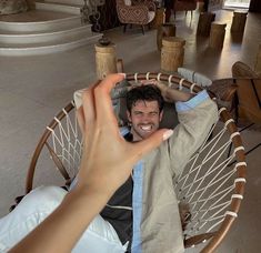 a man sitting in a hammock holding his hand up to the camera and smiling