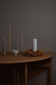 three candles are sitting on a table next to a bowl and some cereal sprouts