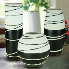 three black and white vases sitting on a table next to each other with flowers in the background