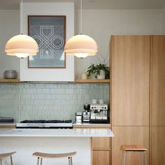 two lights hanging over a kitchen island with stools next to it in front of a counter