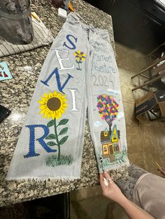 two jeans with embroidered words and sunflowers are sitting on a counter top next to another pair of scissors