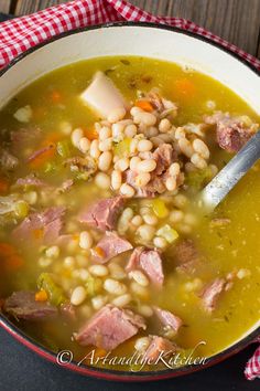 a bowl of soup with ham, beans and carrots in it on a wooden table