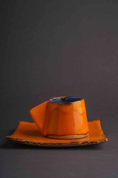 an orange hat sitting on top of a piece of wood next to a cup and saucer