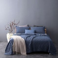 a bed with blue comforters and pillows in a room next to a vase filled with flowers