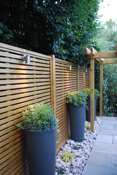 three large planters are next to a wooden fence with rocks and plants in them