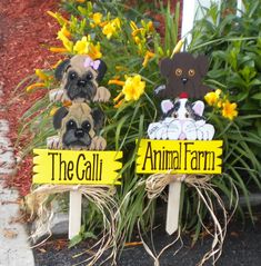 two fake dogs sitting on top of wooden signs in front of flowers and grass with the words the galloi animal farm