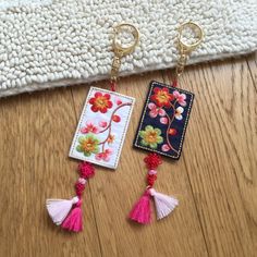 two key chains with flowers and tassels hanging from them on a wooden floor