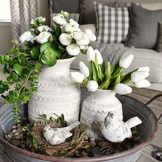 two white vases filled with flowers on top of a table next to a bird's nest