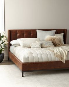 a bed with white and brown pillows on top of it next to a vase filled with flowers