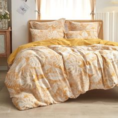 a bed with yellow comforters and pillows in a room next to a window,