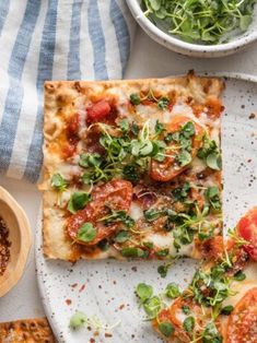 two slices of pizza sitting on top of a white plate next to a bowl of salad