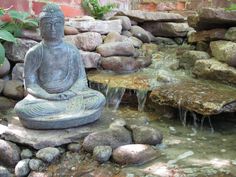 a buddha statue sitting in the middle of a small pond filled with rocks and water