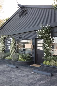 an exterior view of a black building with white flowers and greenery on the windows