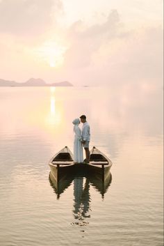 a man and woman are standing on a boat in the middle of the water at sunset