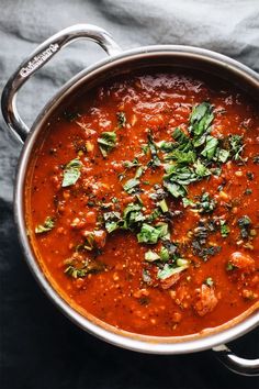 a pot filled with red sauce and garnished with herbs