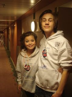 two young people standing next to each other in a hallway with lights on the ceiling