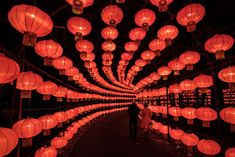 many red lanterns are hanging from the ceiling in this dark room with people standing under them