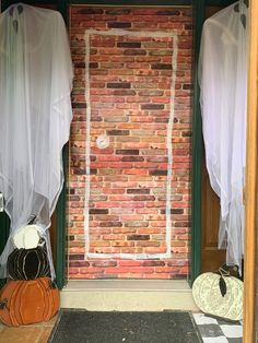 two pumpkins sitting in front of a brick wall with sheer curtains on the windows