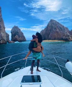 two people are hugging on the back of a boat in front of some rocks and water