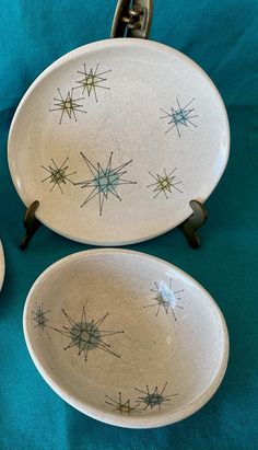 two white dishes with designs on them sitting on a blue tableclothed surface next to each other