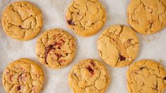 nine cookies with cranberry toppings sitting on top of a white paper lined baking sheet