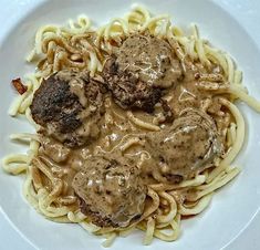 a white plate topped with pasta and meatballs covered in gravy on top of it