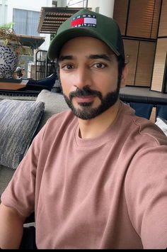 a man with a beard wearing a hat and looking at the camera while sitting on a couch