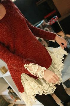 a woman in a red sweater and white lace skirt is holding a cell phone while wearing black tights