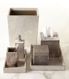 three silver bathroom accessories on a white marble counter top, including tissue dispenser and soap dispenser