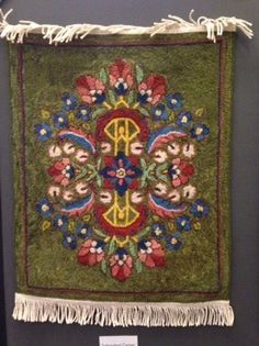 an embroidered wall hanging with fringes and flowers on green ground, in front of a black background