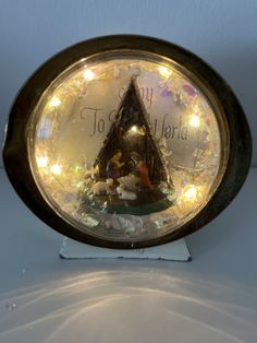 a snow globe with an illuminated christmas tree and nativity scene in the center, on a white surface