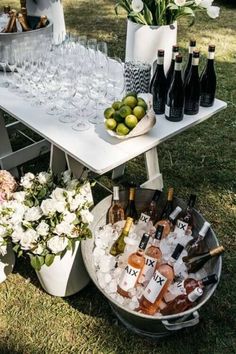 a table with wine bottles and glasses on it in the grass next to some flowers