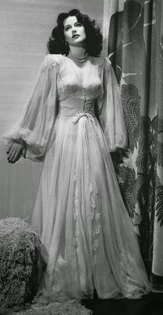 an old photo of a woman in a long white dress standing next to a curtain