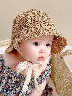 a baby wearing a hat sitting on top of a bed next to a basket and pillow